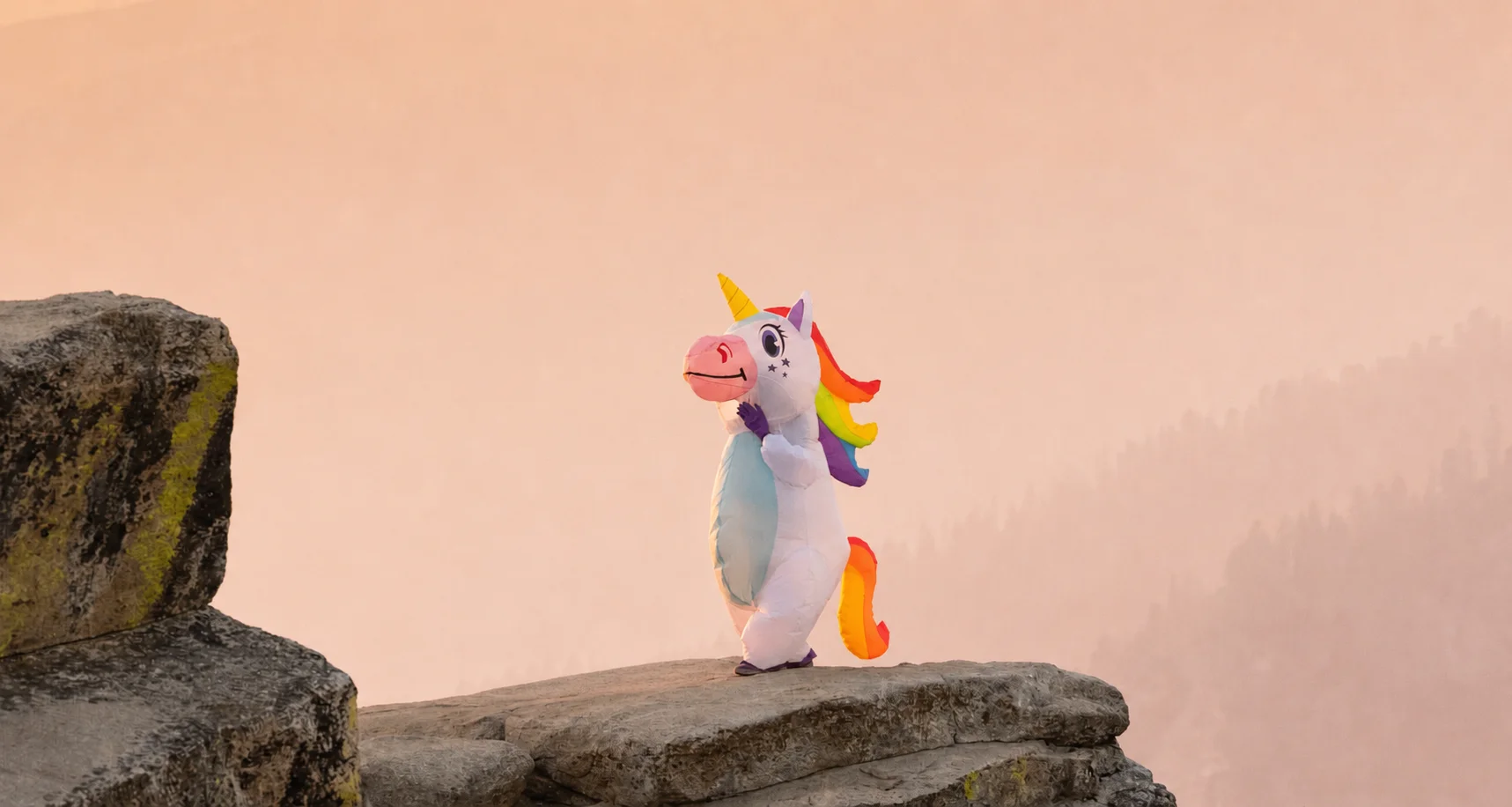 Hero de Paradise Despedidas — escena cinematográfica con unicornio inflable y persona en mono naranja sobre acantilado al atardecer